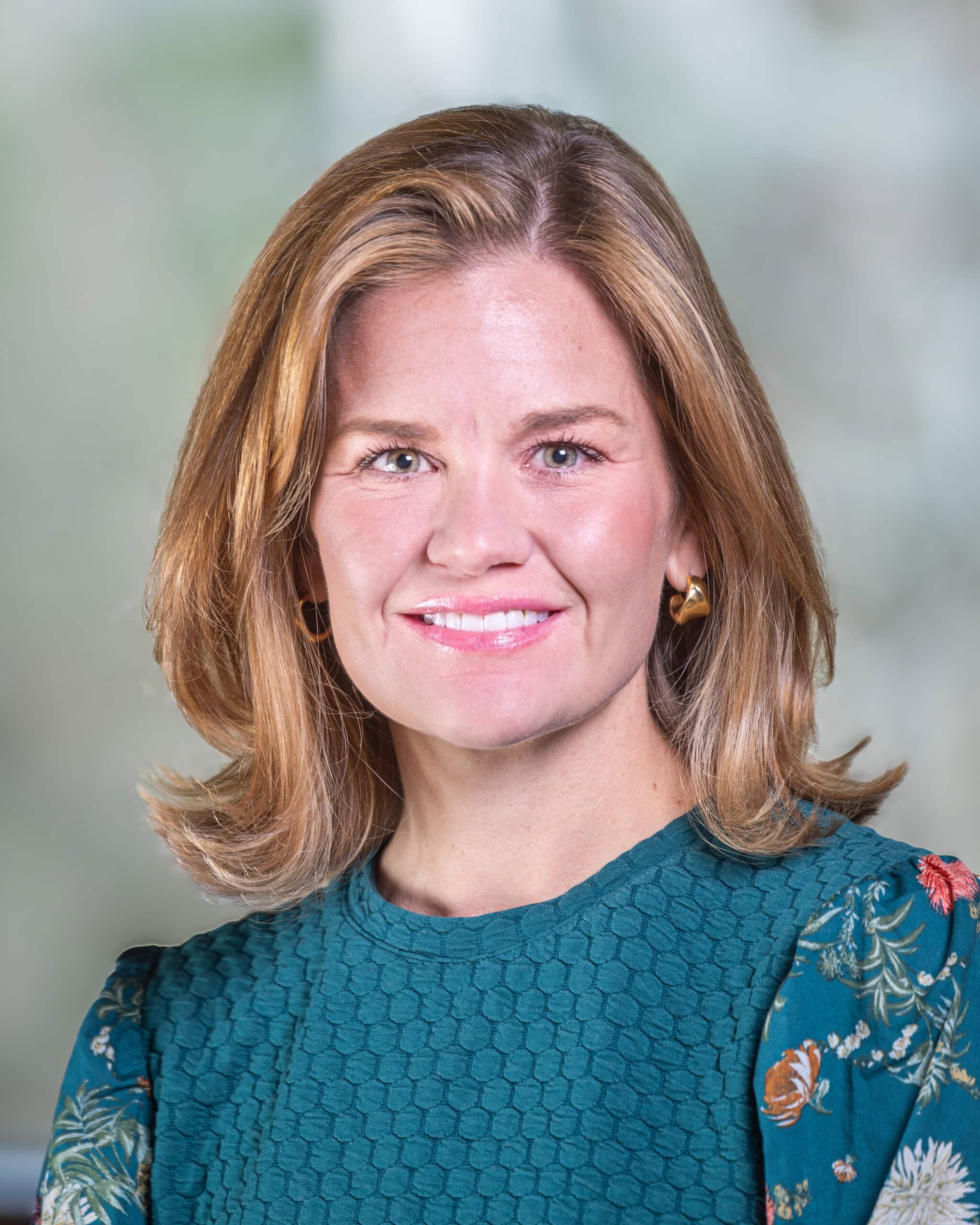 Sarah Griffin, a woman with shoulder length blonde hair wearing a teal blue shirt and smiling at the camera.