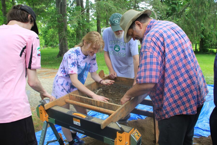 A group of students and faculty sifting dirt at the Granger house