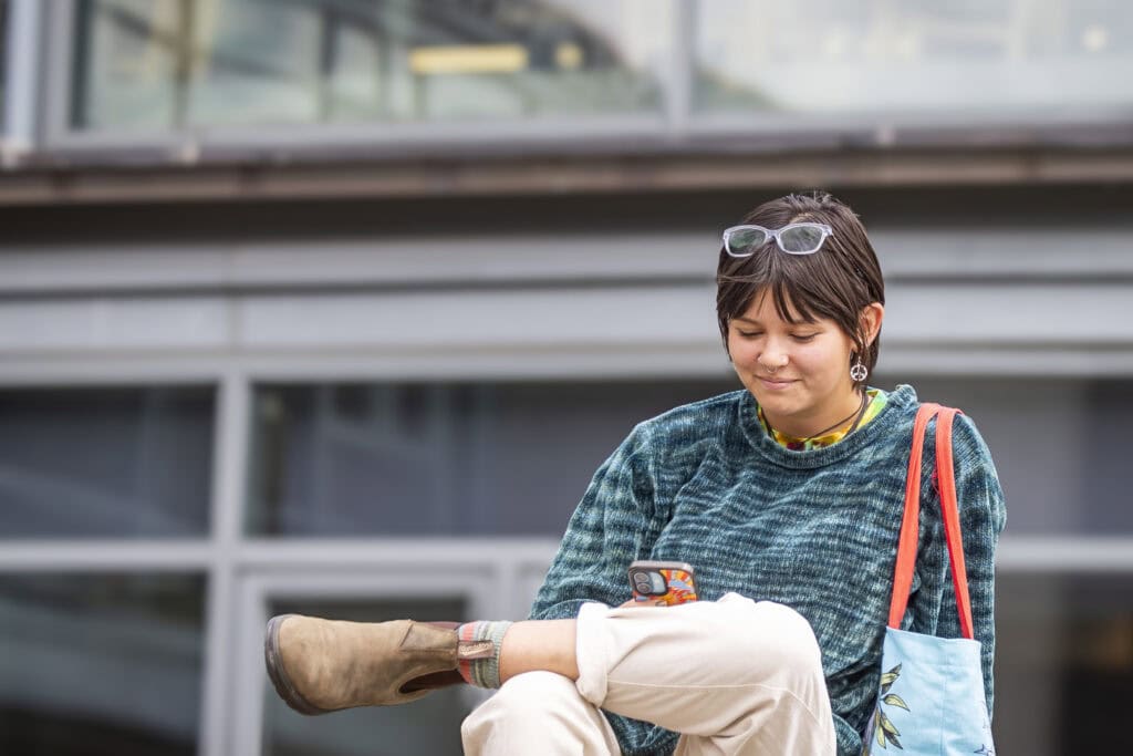 A student sitting outside and scrolling on their cell phone.