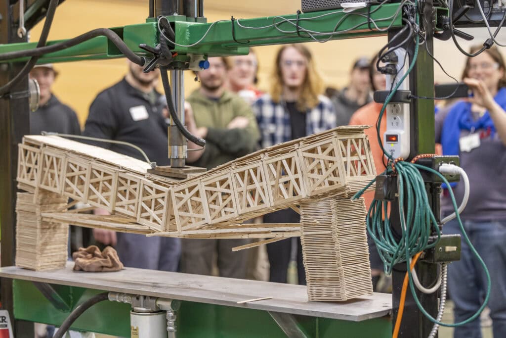 A bridge made out of popsicle sticks and glue cracking in half under the weight of a hydraulic press.
