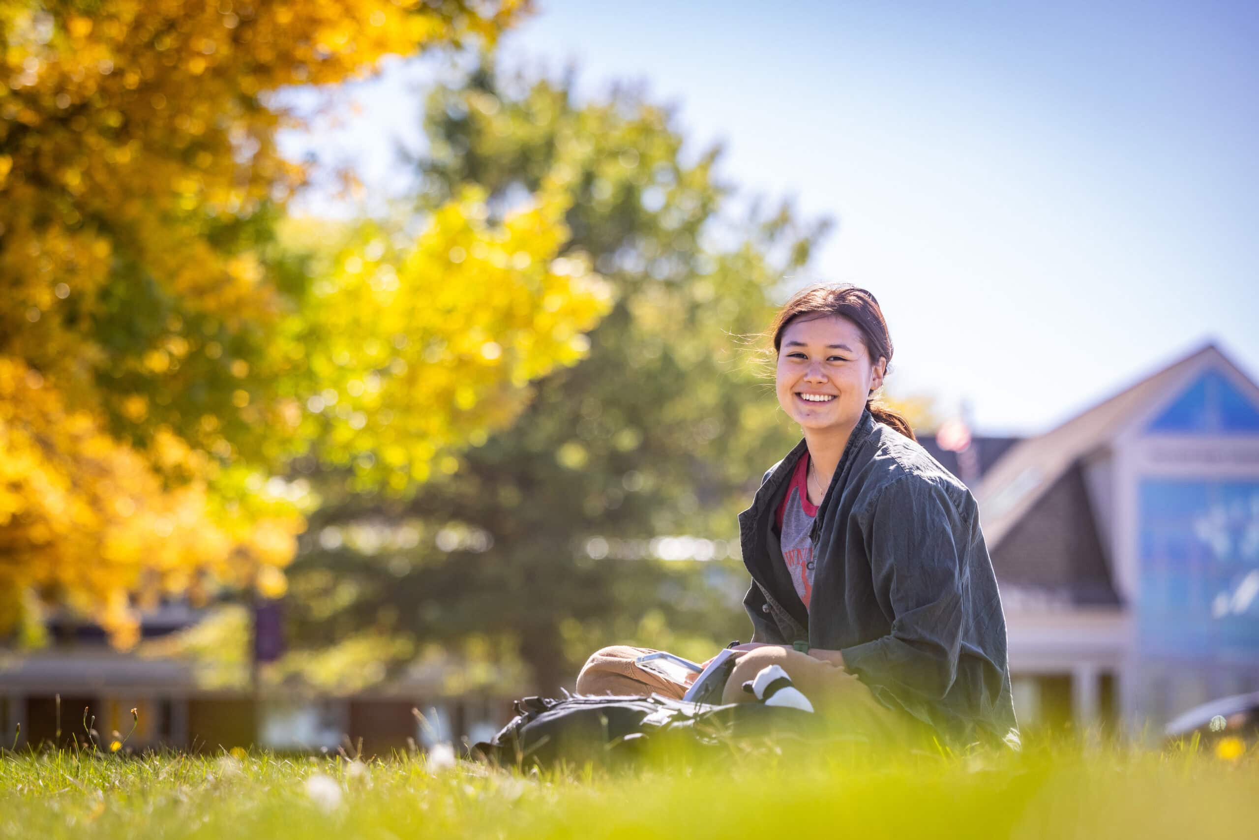 A student sits outside to work on campus during peak fall foliage
