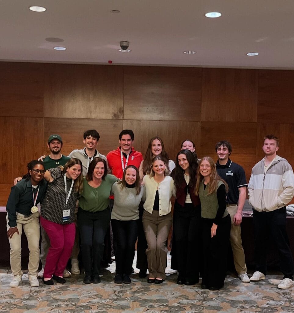 A large group of Master of Athletic Training students and faculty pose together in a conference room for a group photo.
