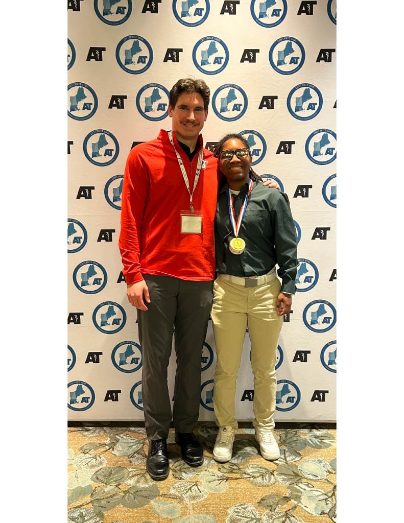 Two students stand together in front of an Eastern Athletic Trainers’ Association backdrop, with one wearing a gold medal on a ribbon.
