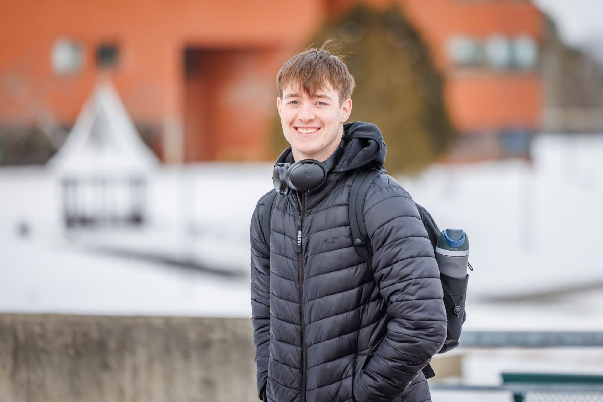 A young man in a black puffy jacket is smiling at the camera on a winter day
