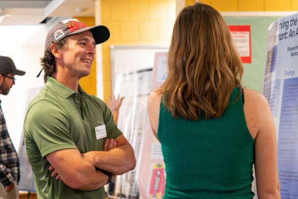 A young woman standing by a research poster and speaking with a faculty member who is smiling at her