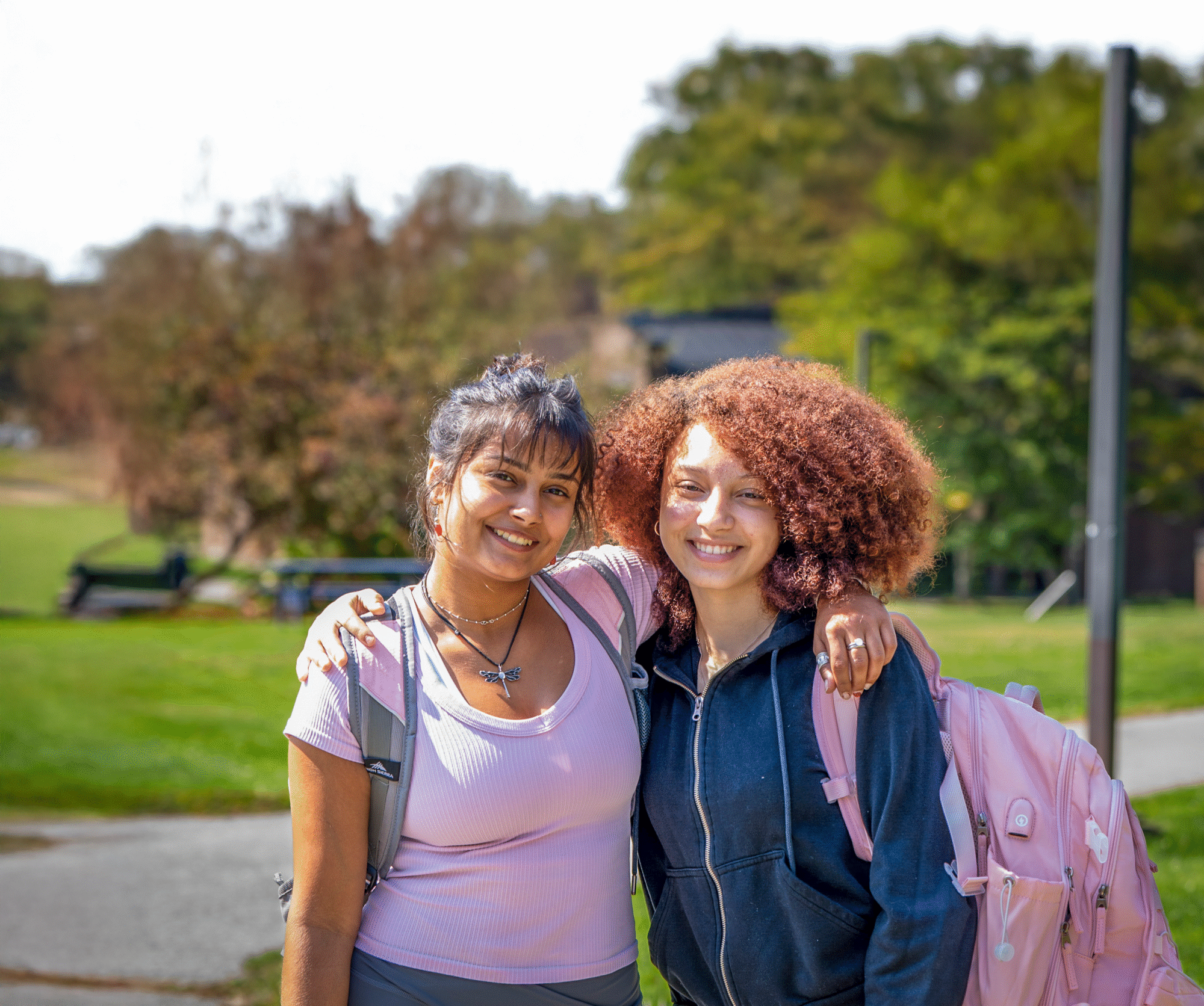 Two students standing side-by-side and smiling on a sunny spring day