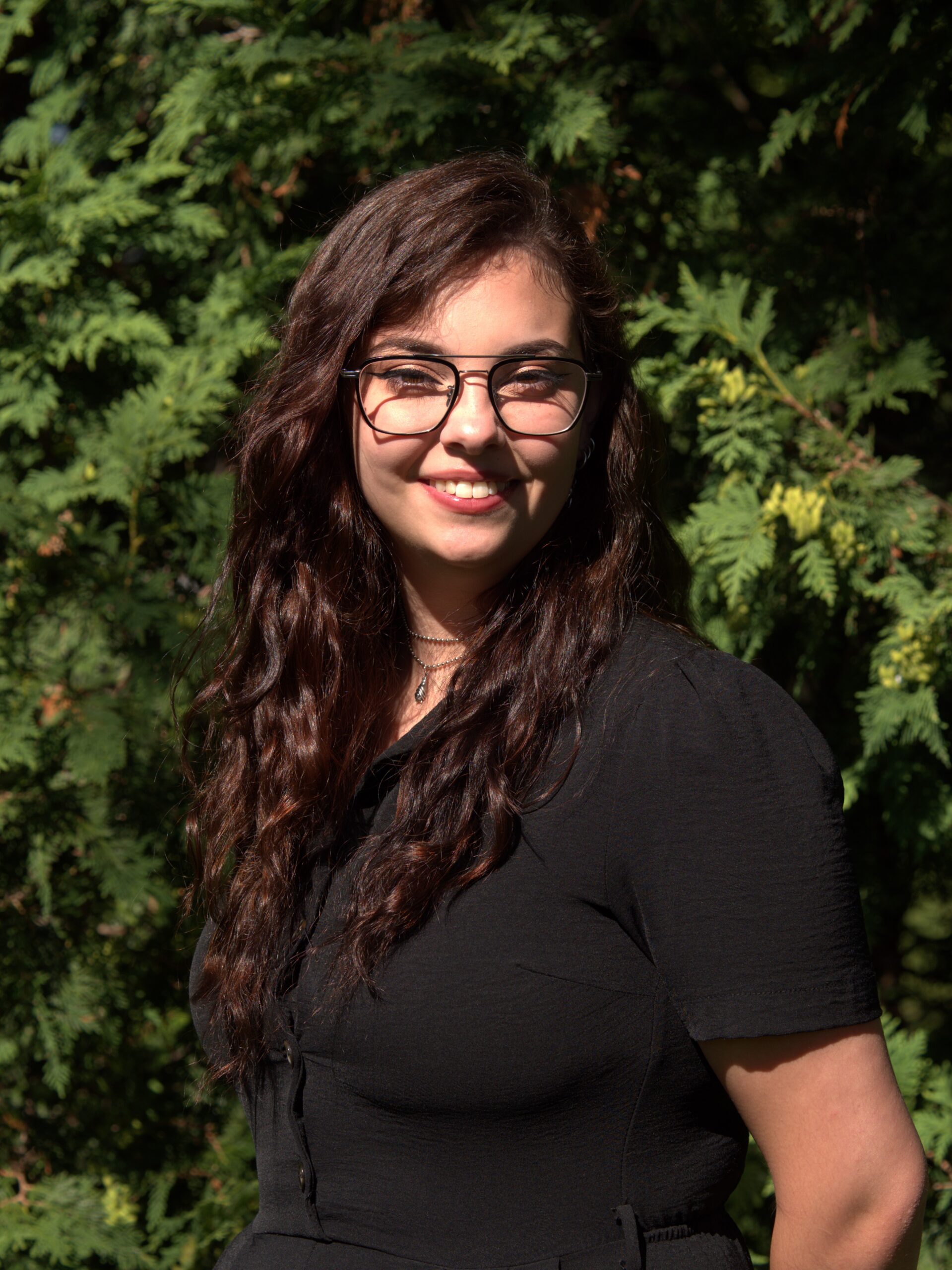 Danielle "Dani" Wright standing outside in front of a fern bush and smiling at the camera