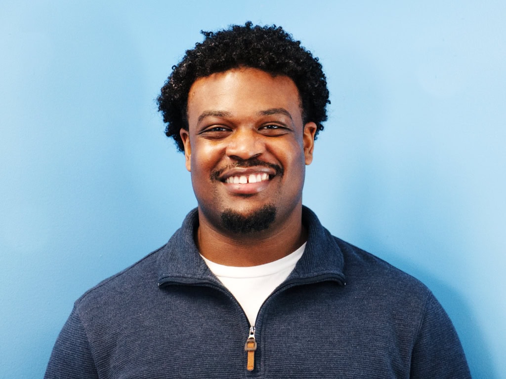 DeVaughn Miller standing inside in front of a light blue wall and smiling at the camera