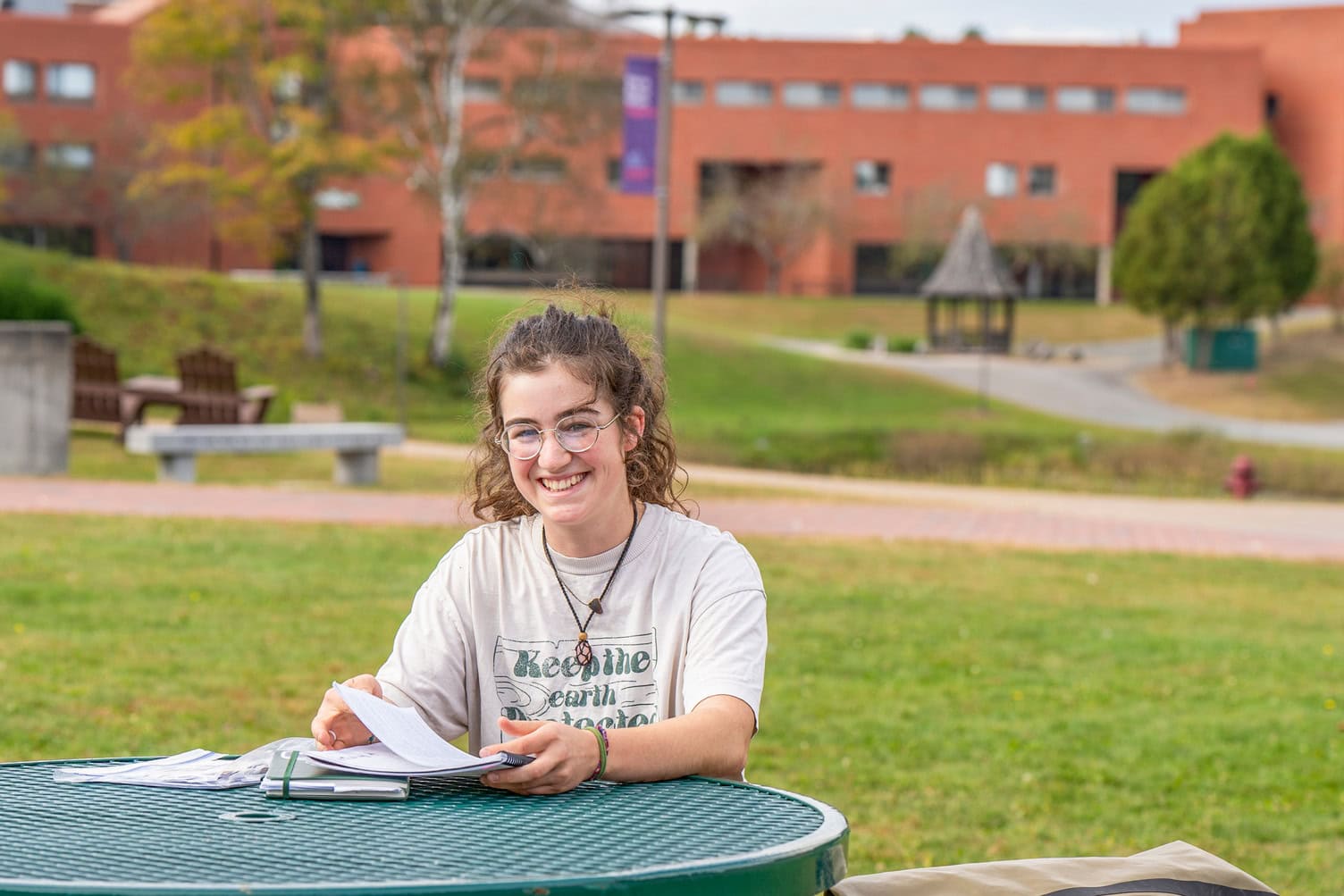 A young woman sitting outside at a round table on a spring day at VTSU Lyndon.