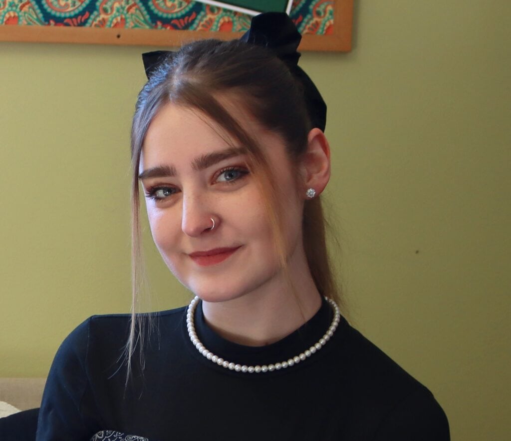 Sky Hulser sitting inside in front of a light green wall and smiling at the camera