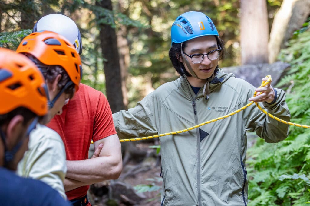 Students wearing protective gear prepare a rope for rock climbing