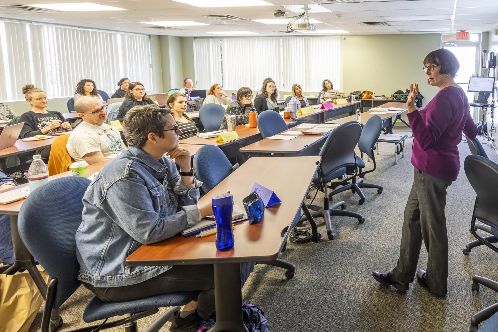 A group of students sitting at long tables in a classroom looking at a faculty member