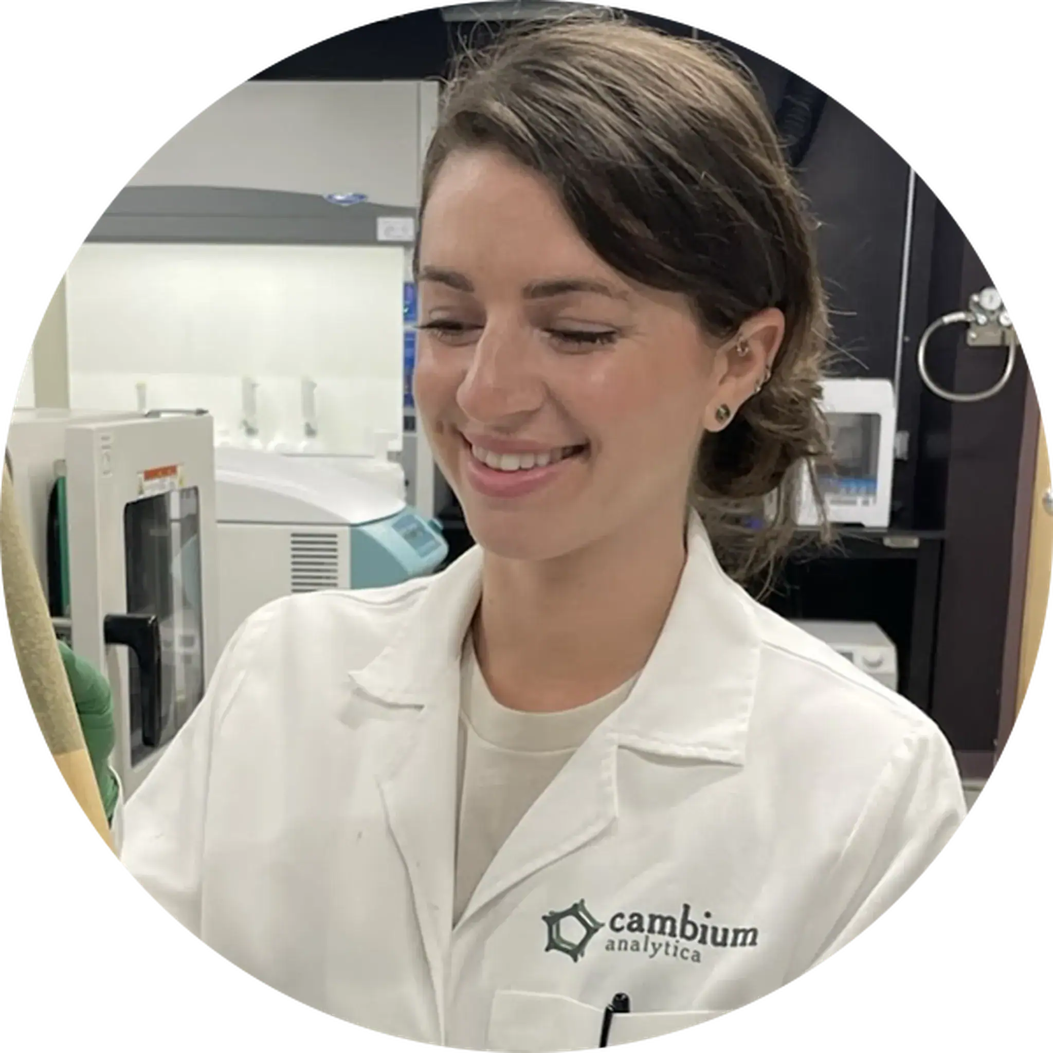 Riley Kirk wearing a white coat in a laboratory and smiling while handling materials