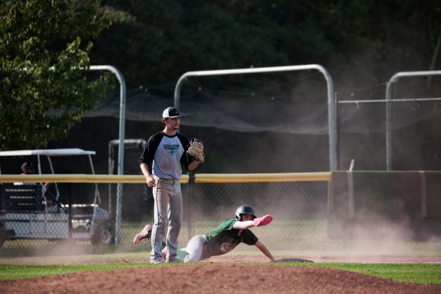 A baseball player sliding on his knees and reaching toward a base while another player stands next to him