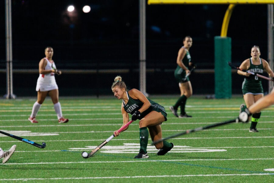 A young woman hitting a ball down the field during a field hockey game