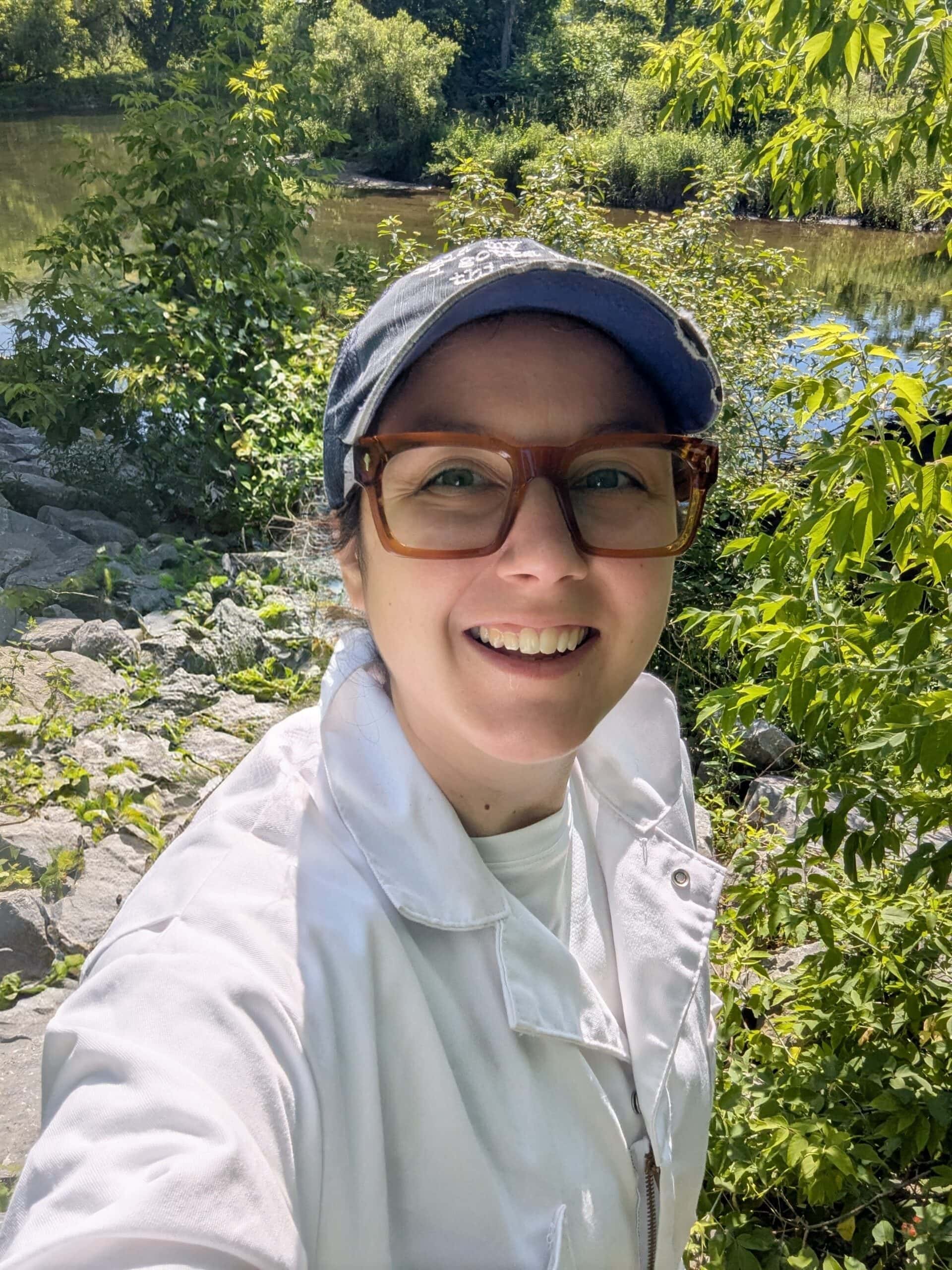 Nik Buonocore standing outside on a sunny day wearing a white button up and a blue ball cap while smiling at the camera.