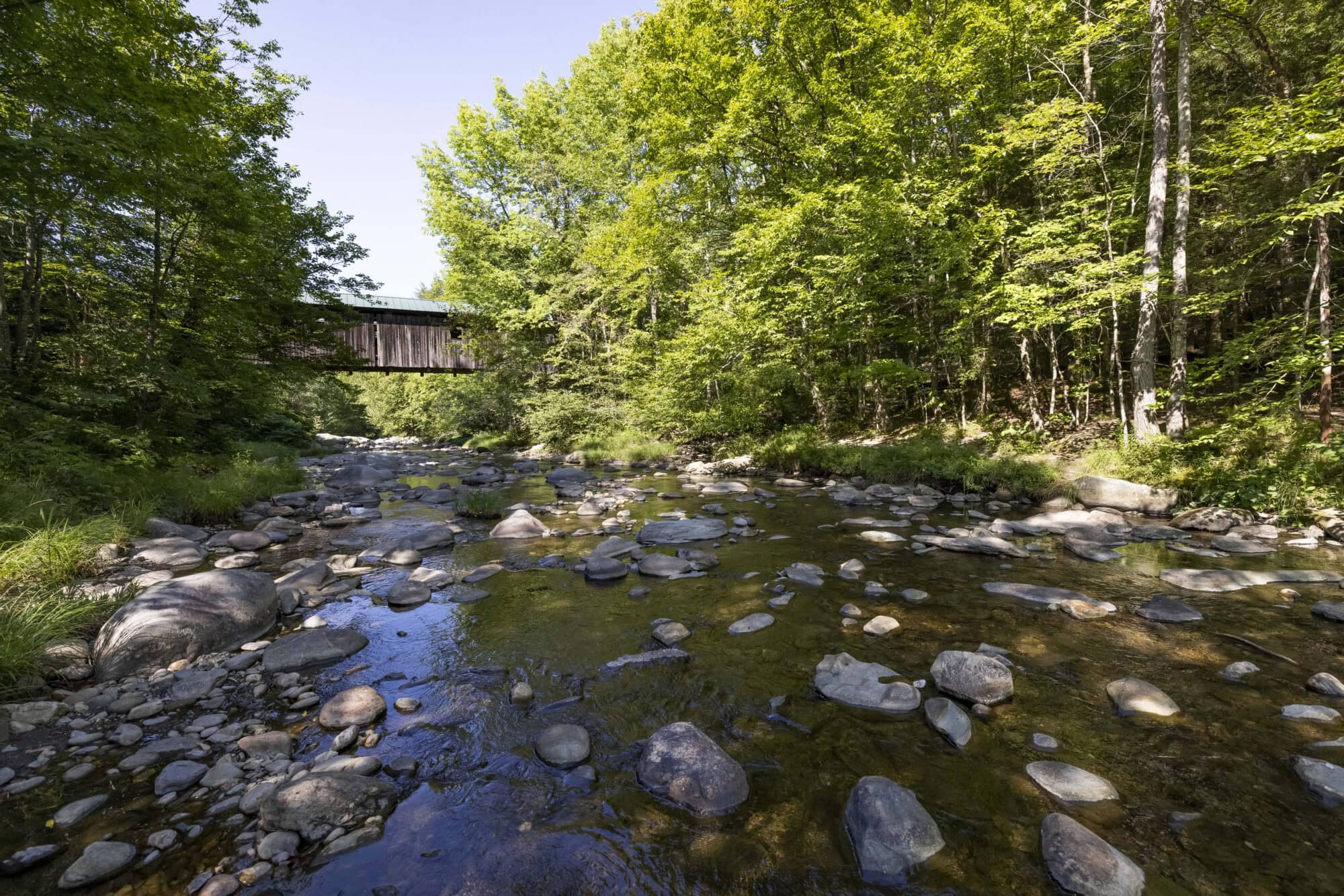 A covered bridge over a rocky river on a bright sunny day