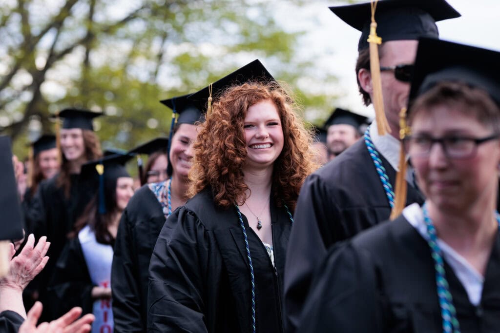 A line of graduates in caps and gowns smiling and walking together