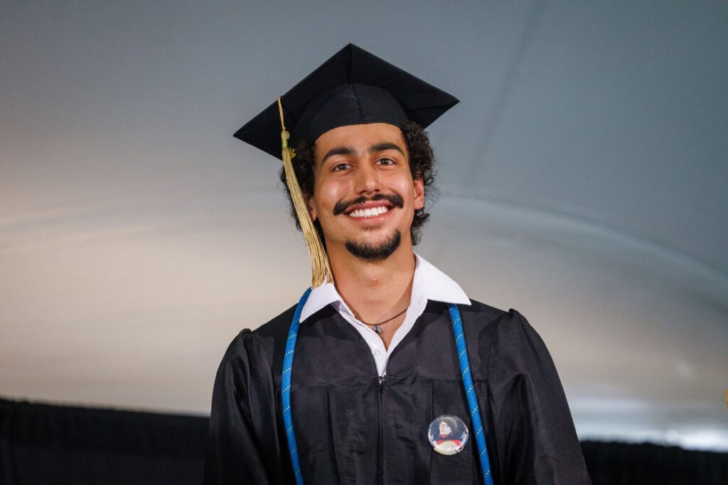 A  young man in graduation cap and gown smiling at the camera