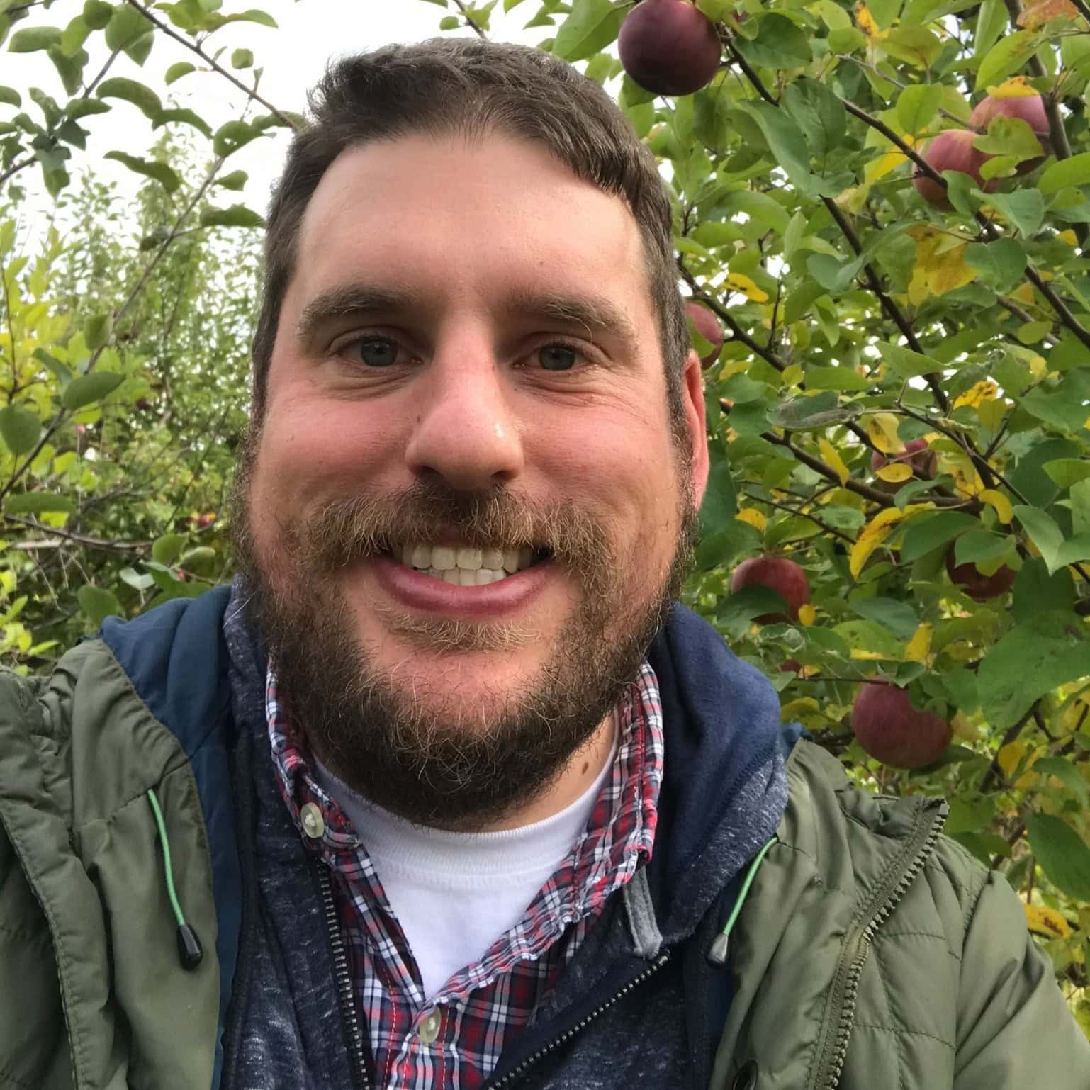 Alex Lenhning standing outside amongst foliage and smiling at the camera