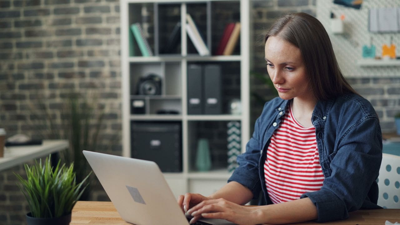 A woman sitting in a home office and working on a laptop