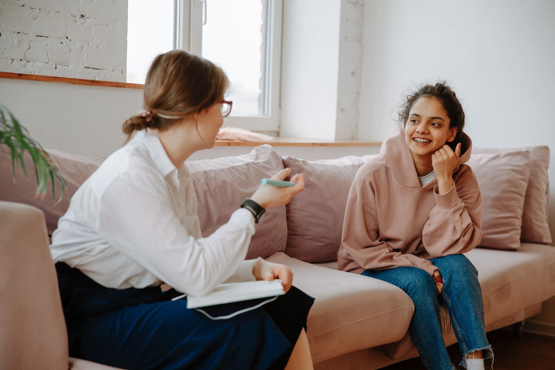 A woman in business clothes sitting on a couch with a school-aged girl talking